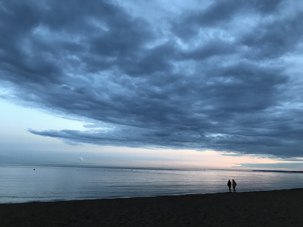 two people standing on a beach under a cloudy sky