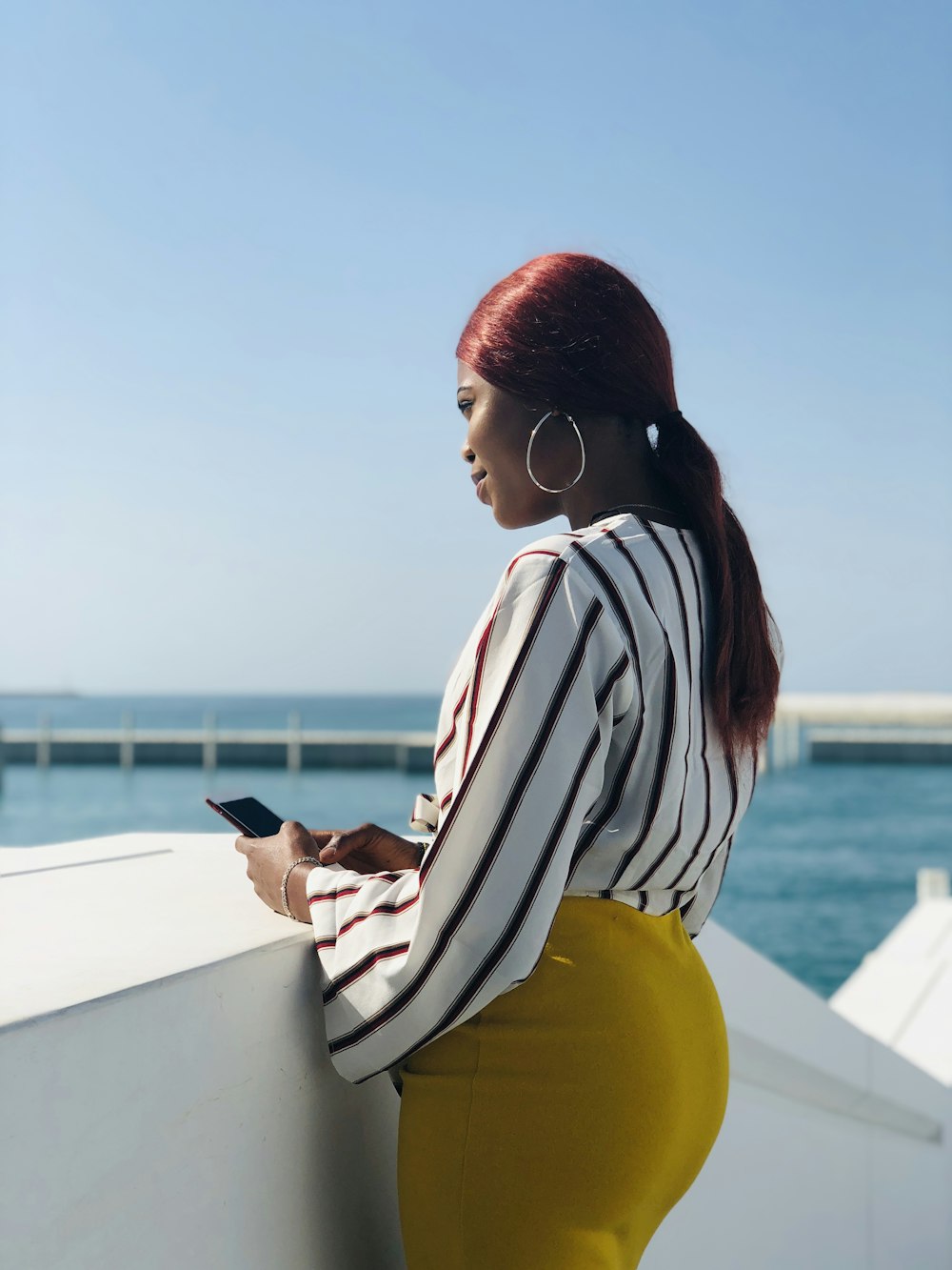 woman in white and maroon striped long-sleeved blouse leaning near wall