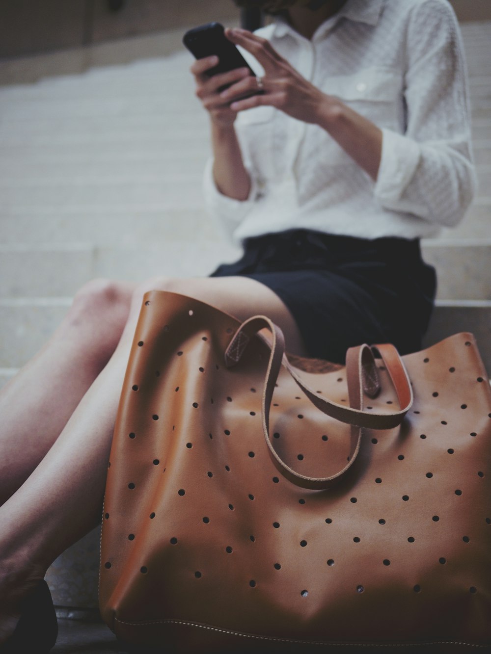 Donna seduta sulla scala di cemento accanto alla borsa di tela in pelle marrone