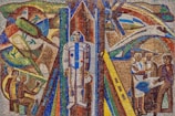 A vibrant mosaic artwork features a central figure in a space suit, surrounded by abstract representations of space exploration elements, including rockets and satellites. On the left, individuals are depicted working with technology, while on the right, a group is engaged in discussion or collaboration. The composition uses bold, geometric patterns and vivid colors to convey a futuristic theme.