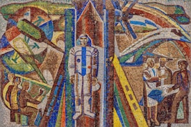 A vibrant mosaic artwork features a central figure in a space suit, surrounded by abstract representations of space exploration elements, including rockets and satellites. On the left, individuals are depicted working with technology, while on the right, a group is engaged in discussion or collaboration. The composition uses bold, geometric patterns and vivid colors to convey a futuristic theme.