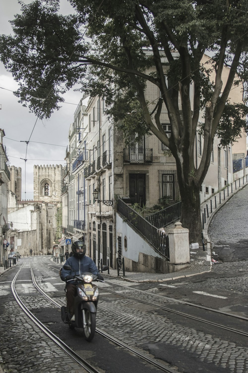 a man riding a motorcycle down a street next to a tree