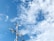 A wind turbine and two solar panels are positioned against a backdrop of a bright blue sky with scattered white clouds.