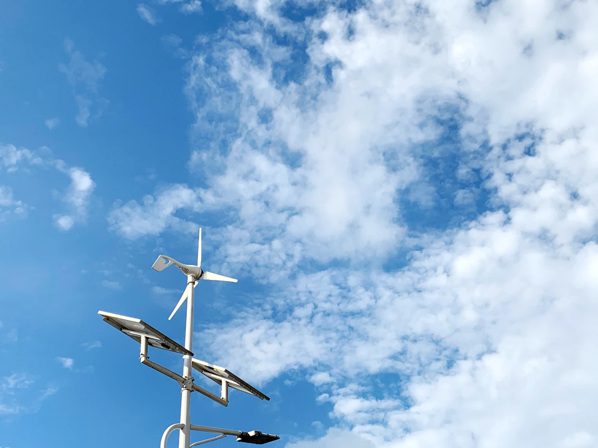 A solar panel field under a bright blue sky with wind turbines in the background.