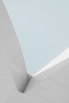 A minimalist architectural structure with clean lines and smooth surfaces. The composition involves a contrast between light grey and soft cyan colors, giving a sense of calm and simplicity.