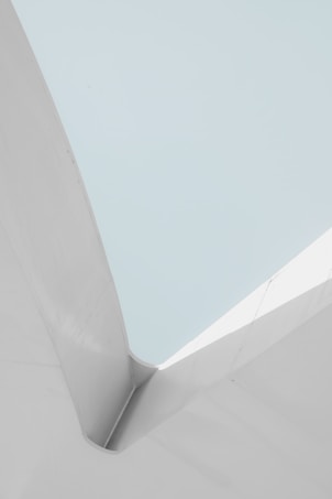 A minimalist architectural structure with clean lines and smooth surfaces. The composition involves a contrast between light grey and soft cyan colors, giving a sense of calm and simplicity.