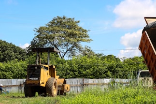 A vibrant side dump truck painted bright yellow parked against a clear blue sky.