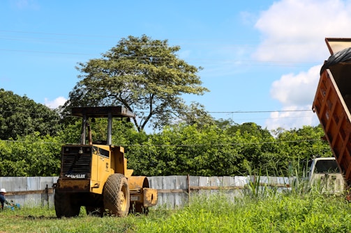 A vibrant side dump truck painted bright yellow parked against a clear blue sky.
