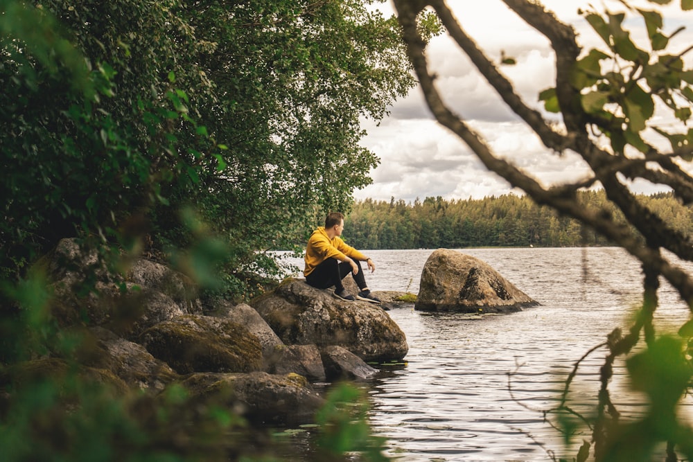 man sitting on rock beside river