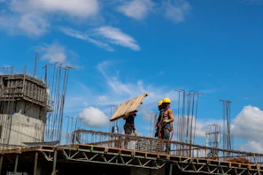 Team members in safety gear discussing plans beside a large earthworks project under a clear blue sky.