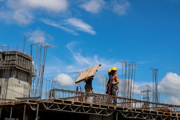 Workers wearing protective equipment collaborating on a construction site under clear skies.