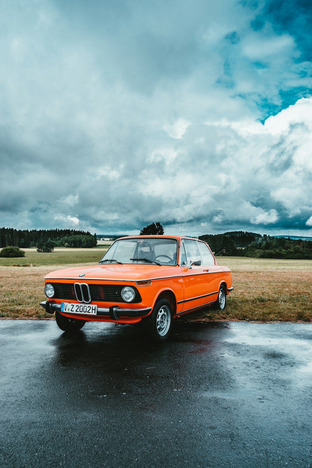 berlina BMW arancione parcheggiata vicino a un campo erboso