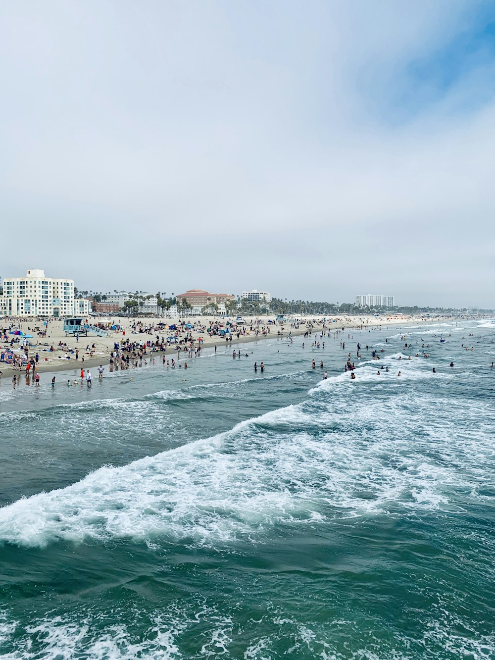 a crowded beach on a cloudy day with people in the water