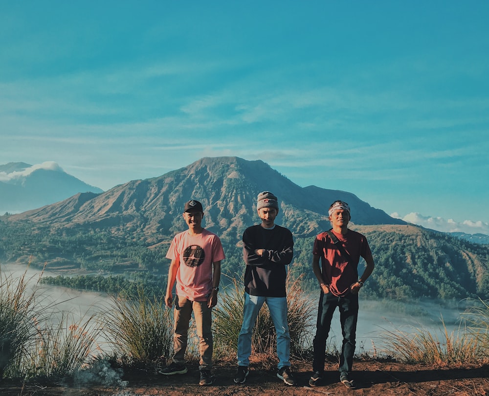 three man standing near mountain under blue sky