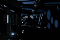 A dark room filled with large circular patterns projected onto the walls and ceiling. The room has several vertical pillars and scattered equipment. Soft blue and black hues dominate the space, creating an abstract and mysterious atmosphere.