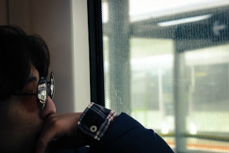 Close-up portrait of a person looking thoughtfully out of a rain-dotted window.