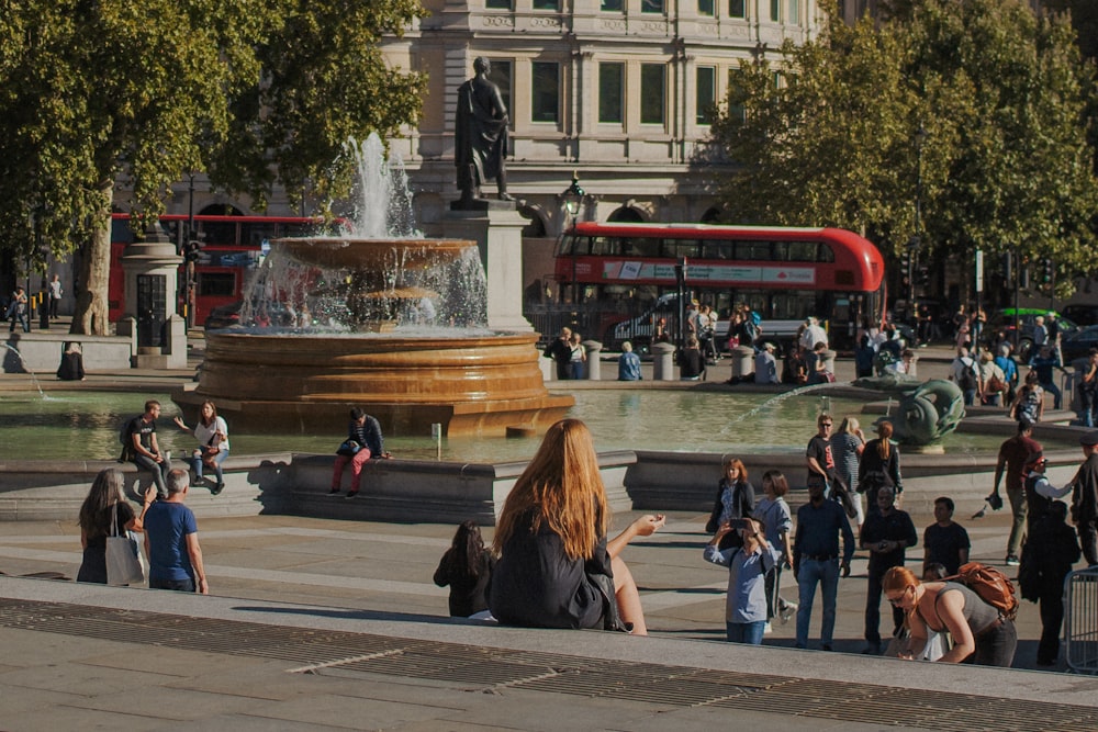 woman in black dress sitting on stair overlooking fountain and people walking