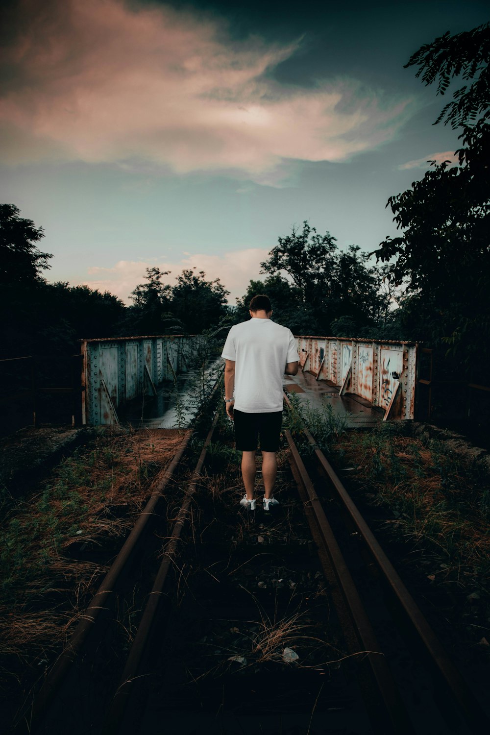 man in white T-shirt and black shorts standing on railway