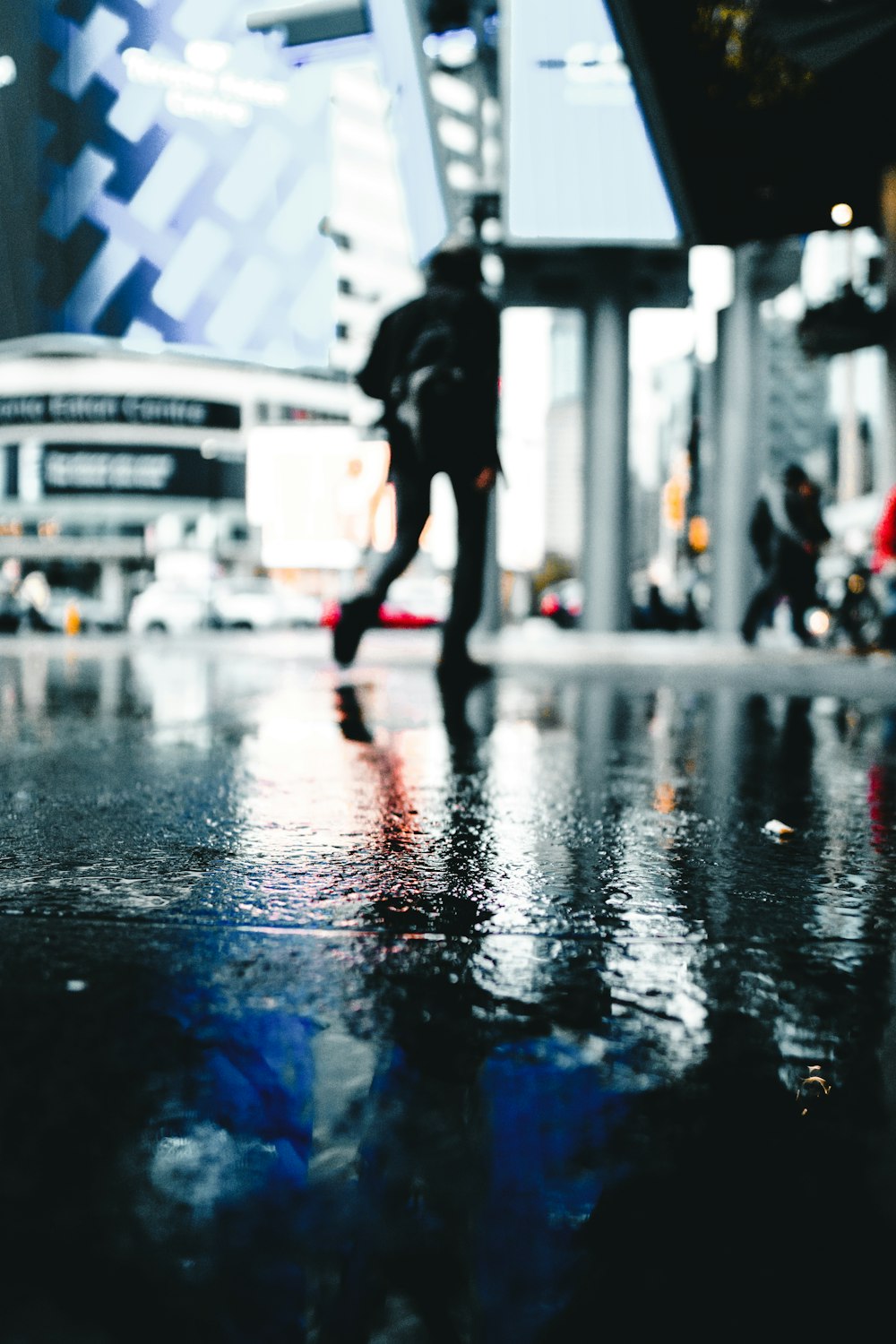 a person walking across a wet street next to a tall building