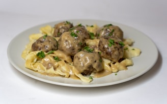 A plate filled with creamy pasta and generously sized meatballs, topped with a rich, smooth sauce and garnished with fresh green herbs.