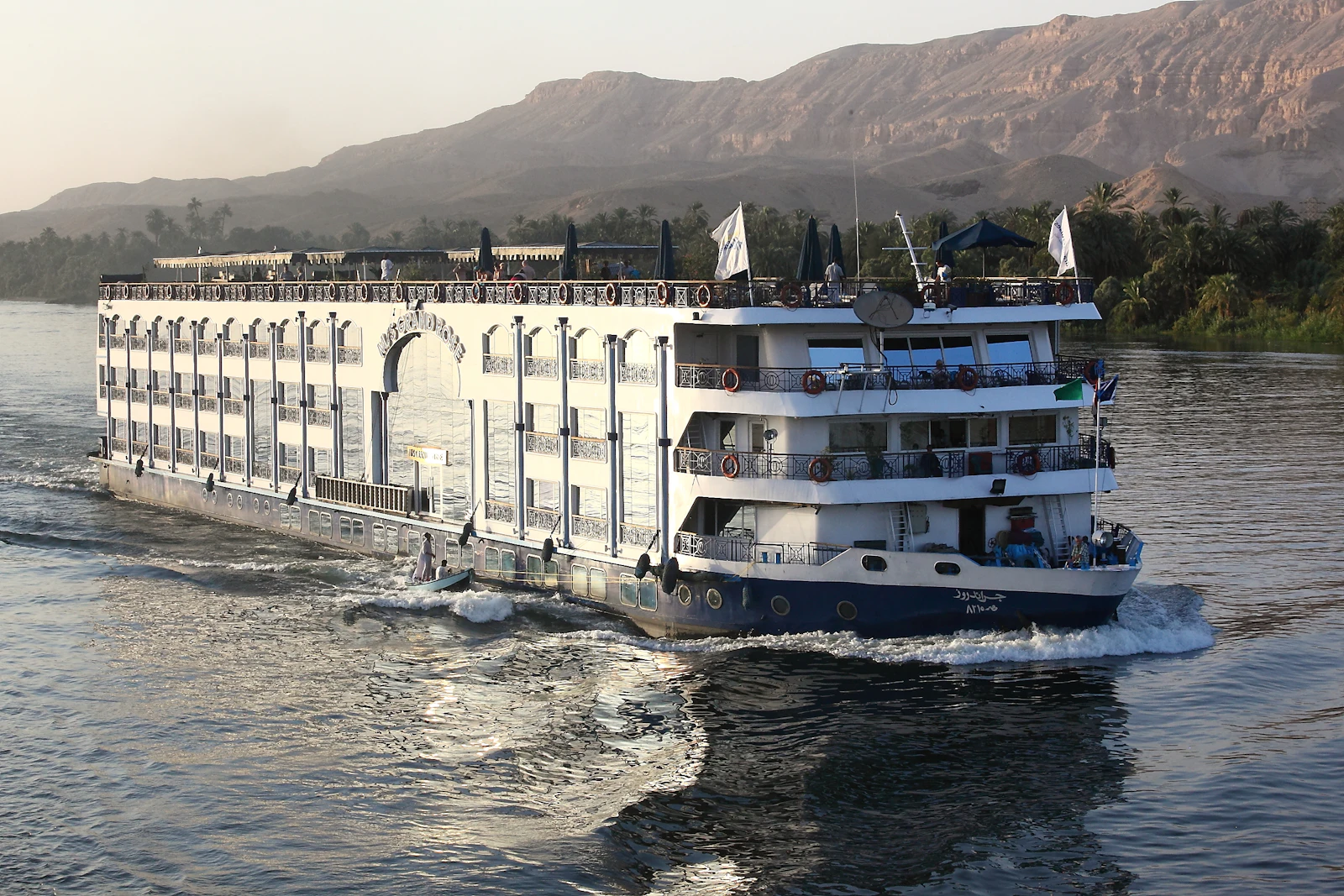 Passengers on the deck of a river cruise ship below mountains