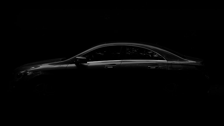 Sleek black sedan parked under soft lighting against a dark backdrop.