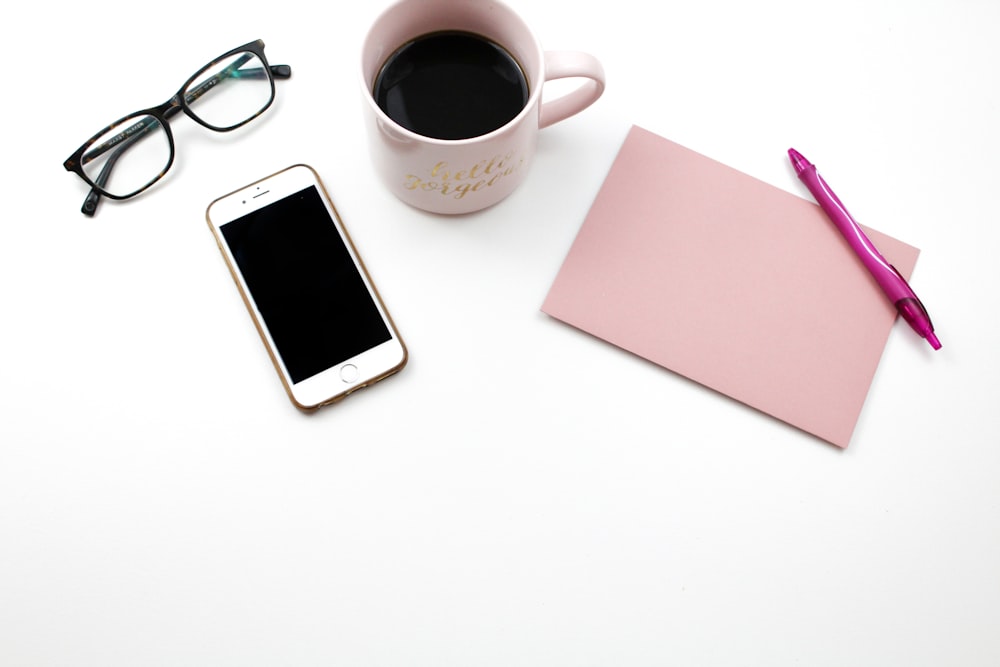 iPhone beside mugs with coffee, eyeglasses, and notes