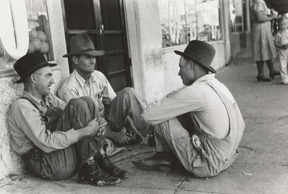 grayscale photo of man wearing cowboy hat sitting in front of door