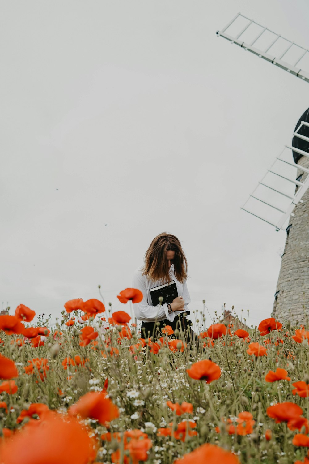 femme portant une chemise blanche tenant un livre noir près d’un moulin à vent