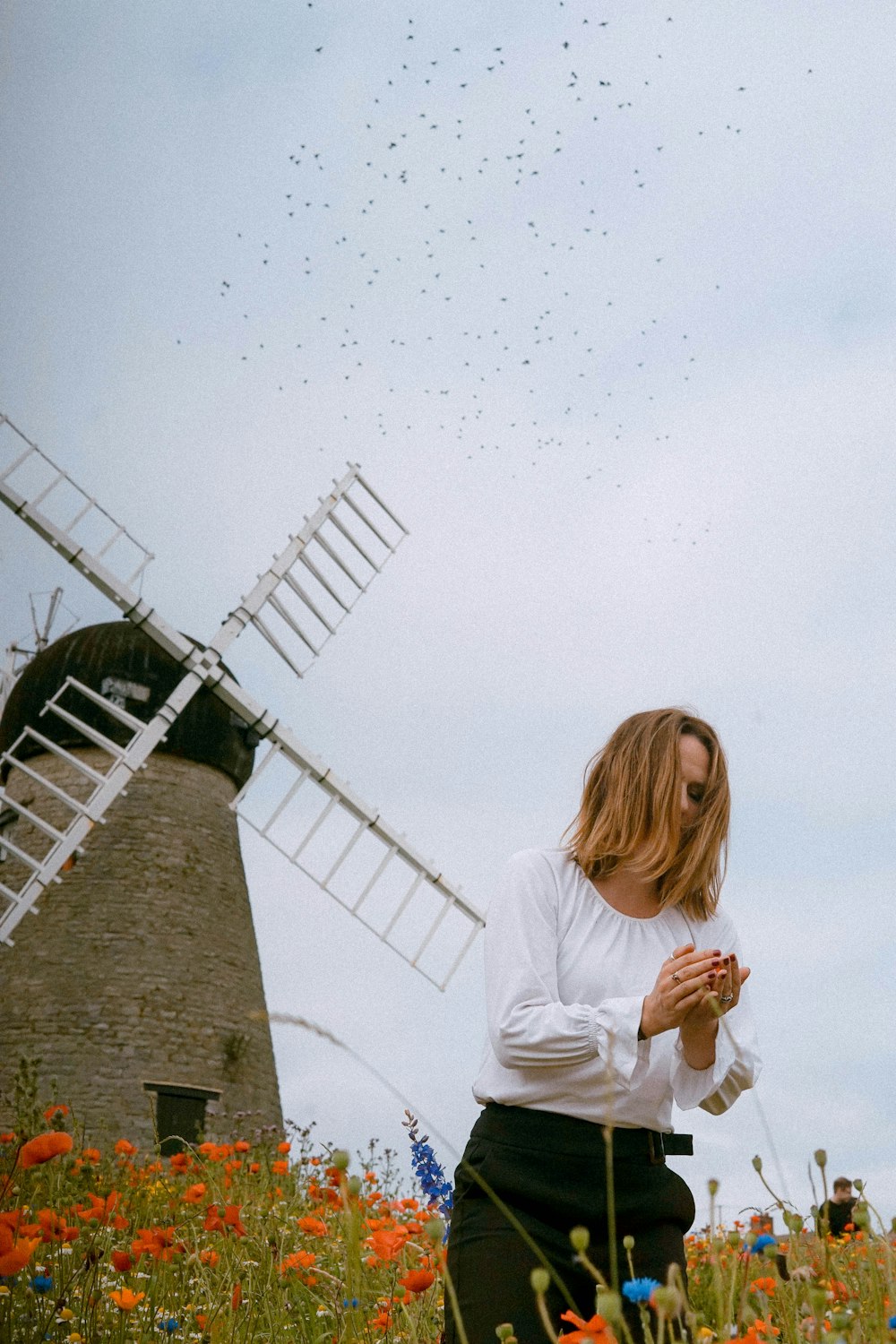 woman wearing white long-sleeved shirt and black pants surrounded by red flowers