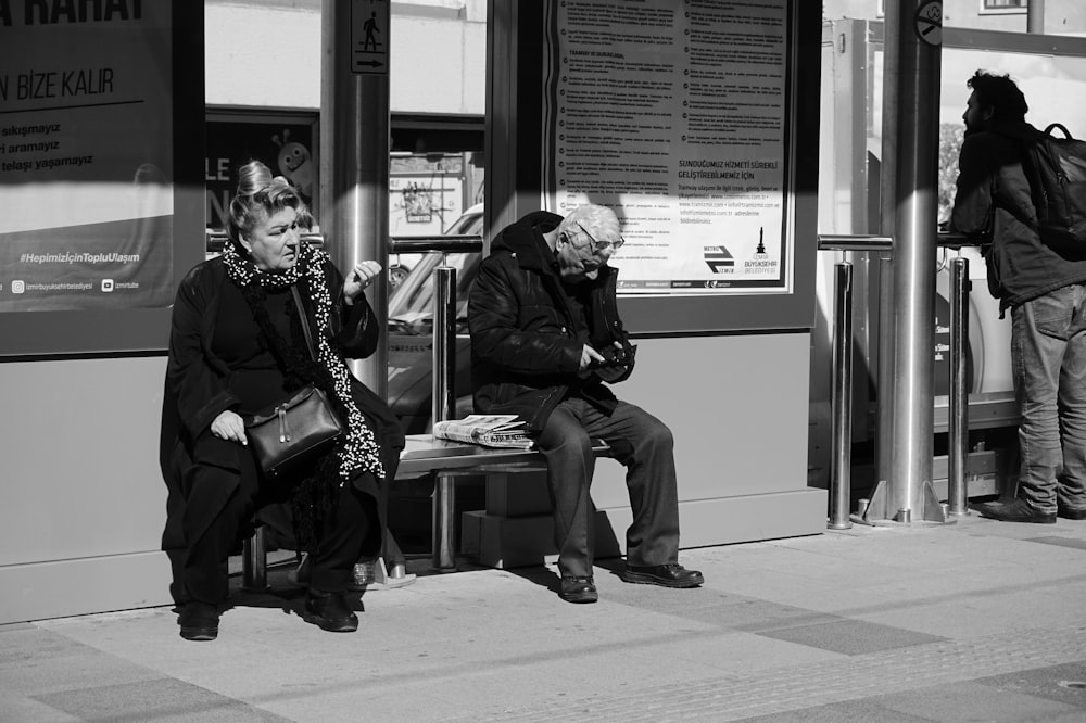 grayscale photo of two person sitting beside structure