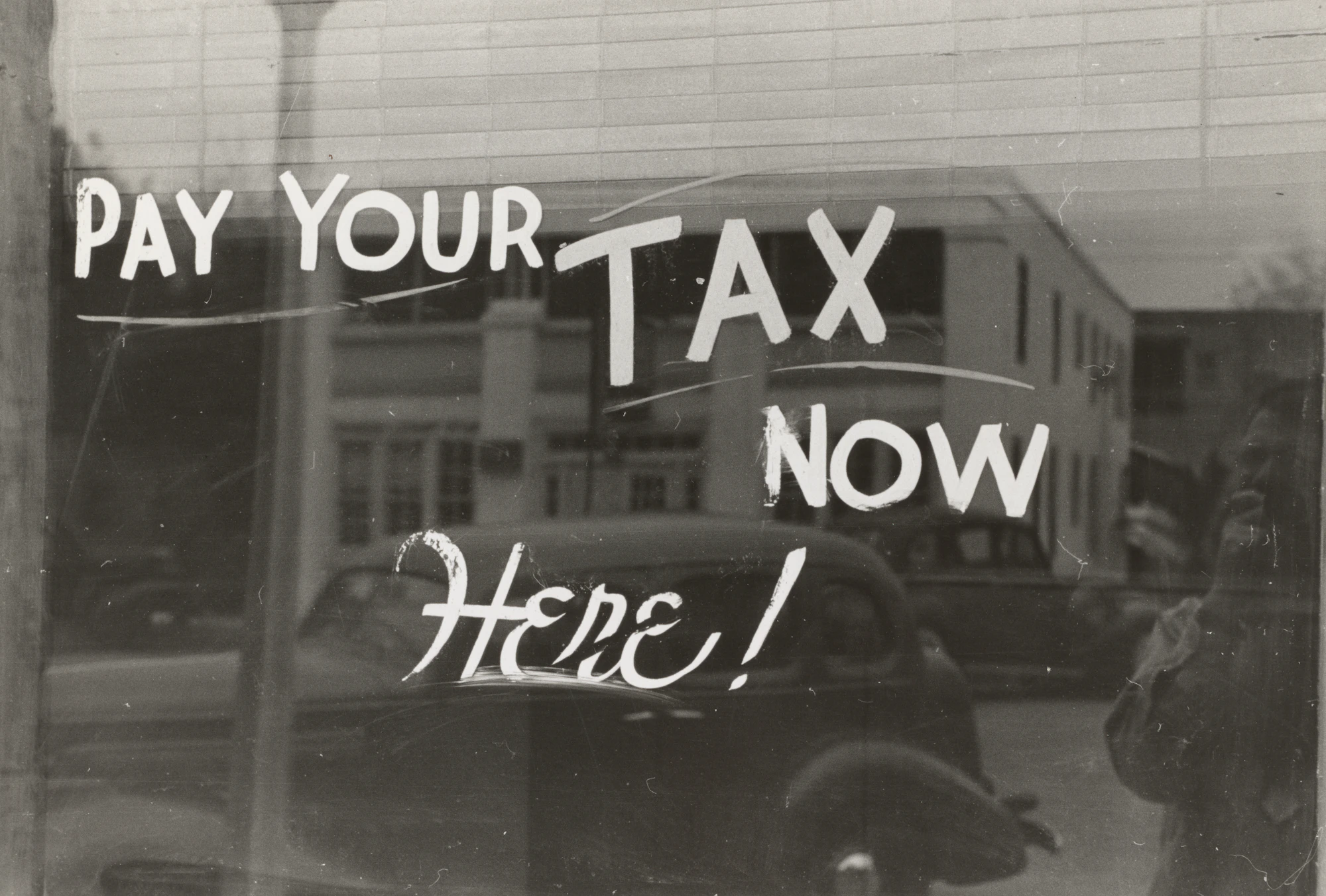 Window display with handwritten text reading PAY YOUR TAX NOW HERE!