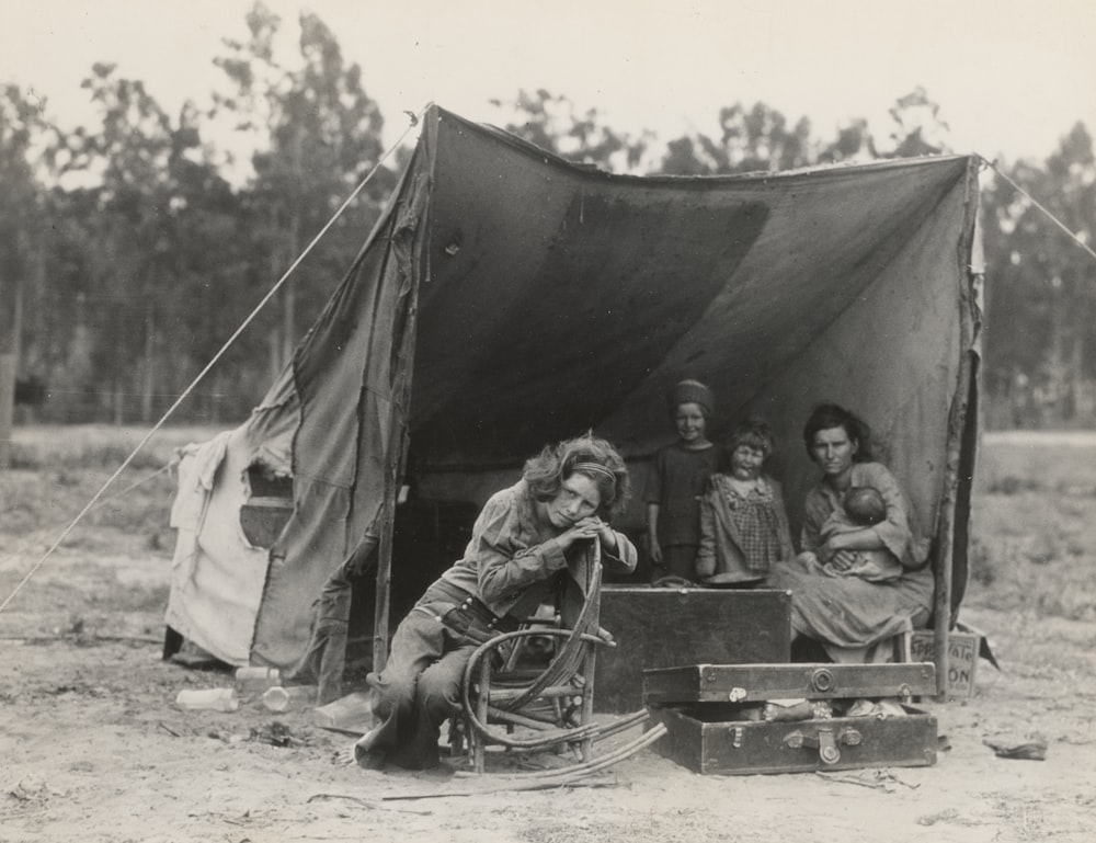 Fotografía en escala de grises de dos mujeres con tres niños bajo una tienda de campaña