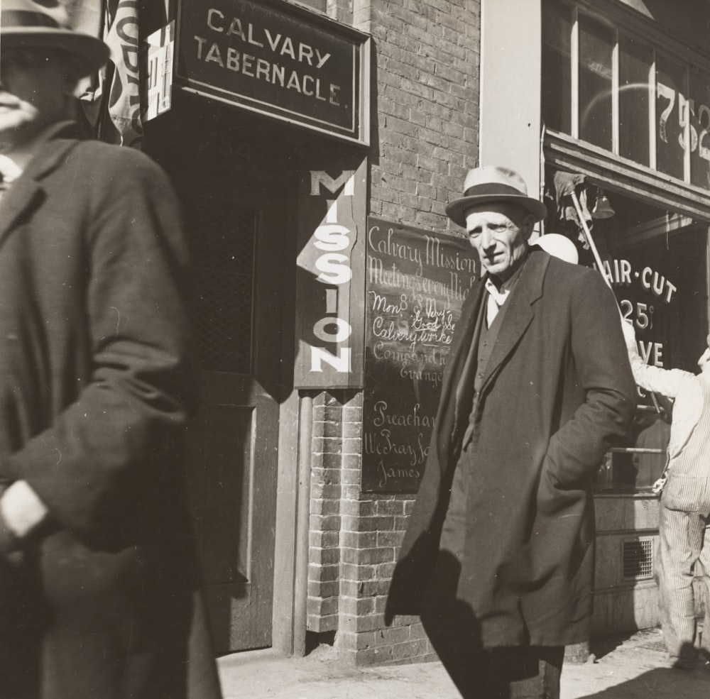 grayscale photo of man walking beside building