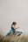 A person in a blue dress is seen twirling amidst tall grass under an overcast sky. The movement suggests a sense of freedom and joy, with the dress flowing and capturing the motion. The background is soft and muted, allowing focus on the graceful motion.