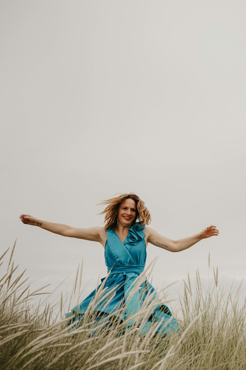 woman jumping on grass while smiling during daytime