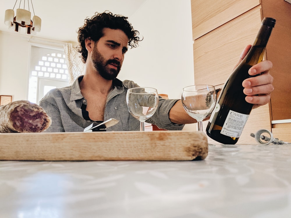 man holding white glass bottle sitting beside table