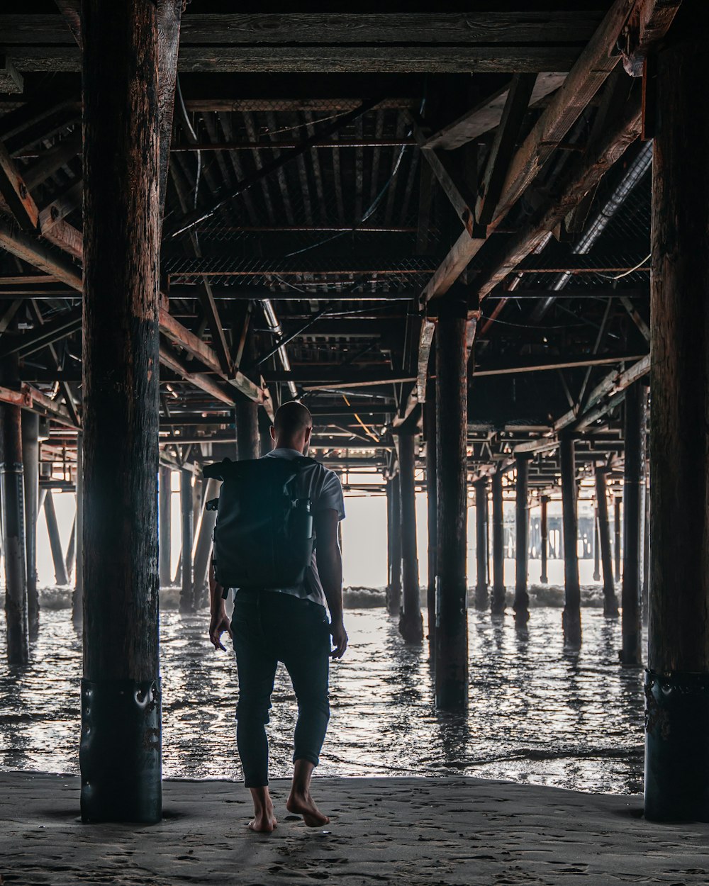 Hombre con camiseta gris y pantalones negros de pie bajo el muelle