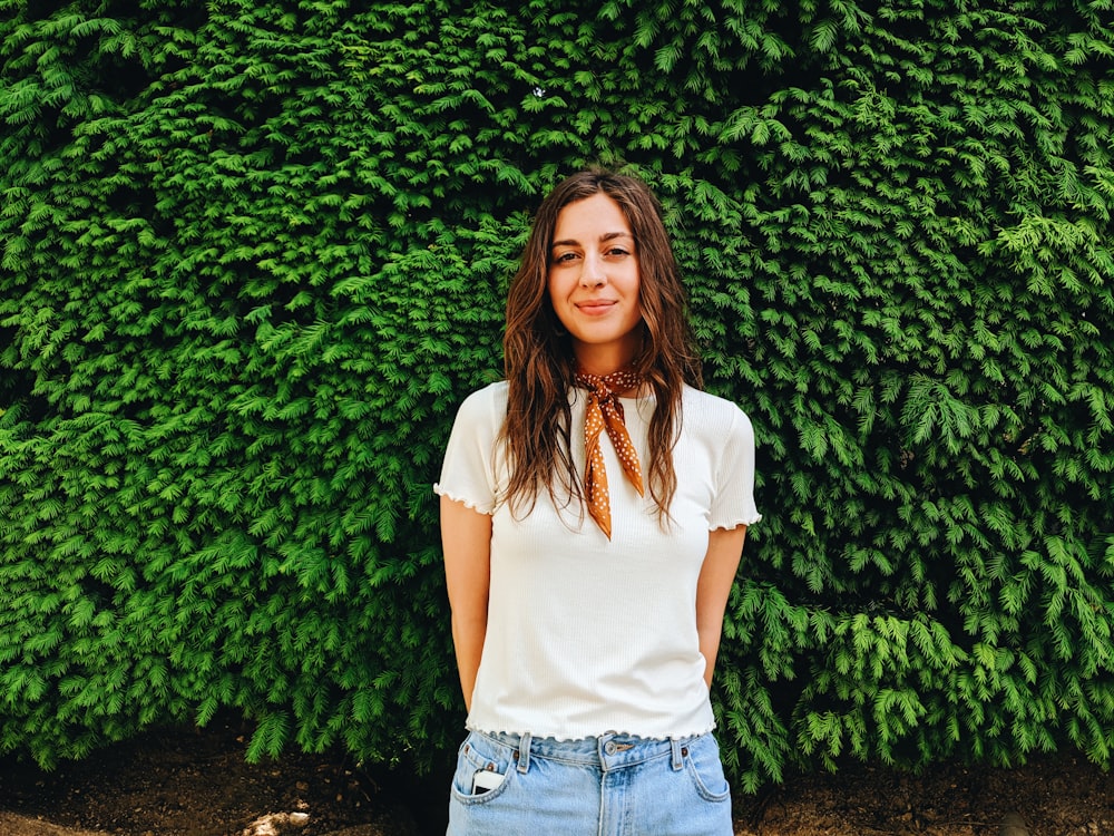 woman in white blouse standing by the green bush and smiling