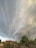 Dramatic, swirling storm clouds fill the sky above a small rural area with houses and trees. Power lines stretch across the scene, and a few people are visible on the ground.