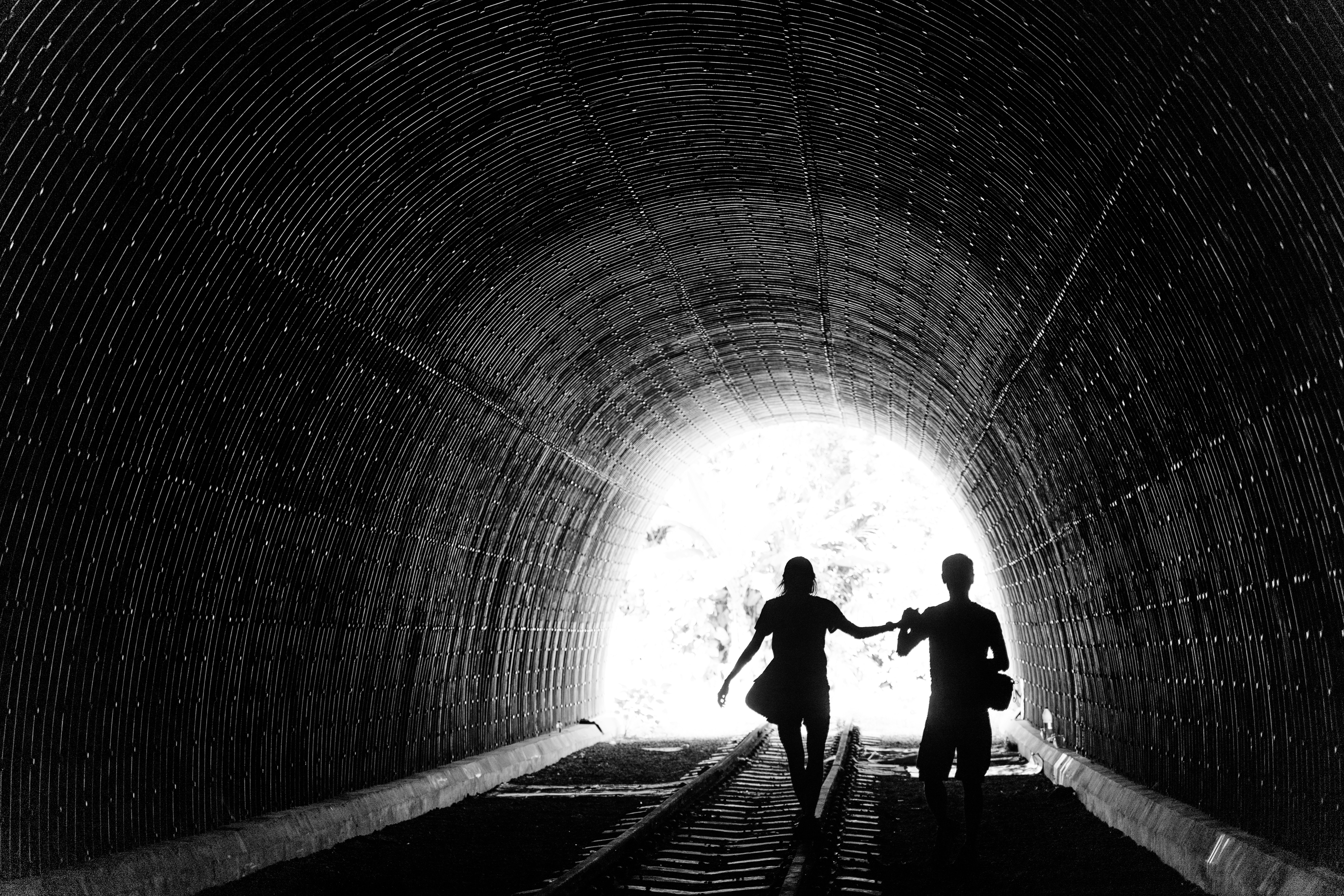 grayscale photo of man and woman holding hands inside tunnel