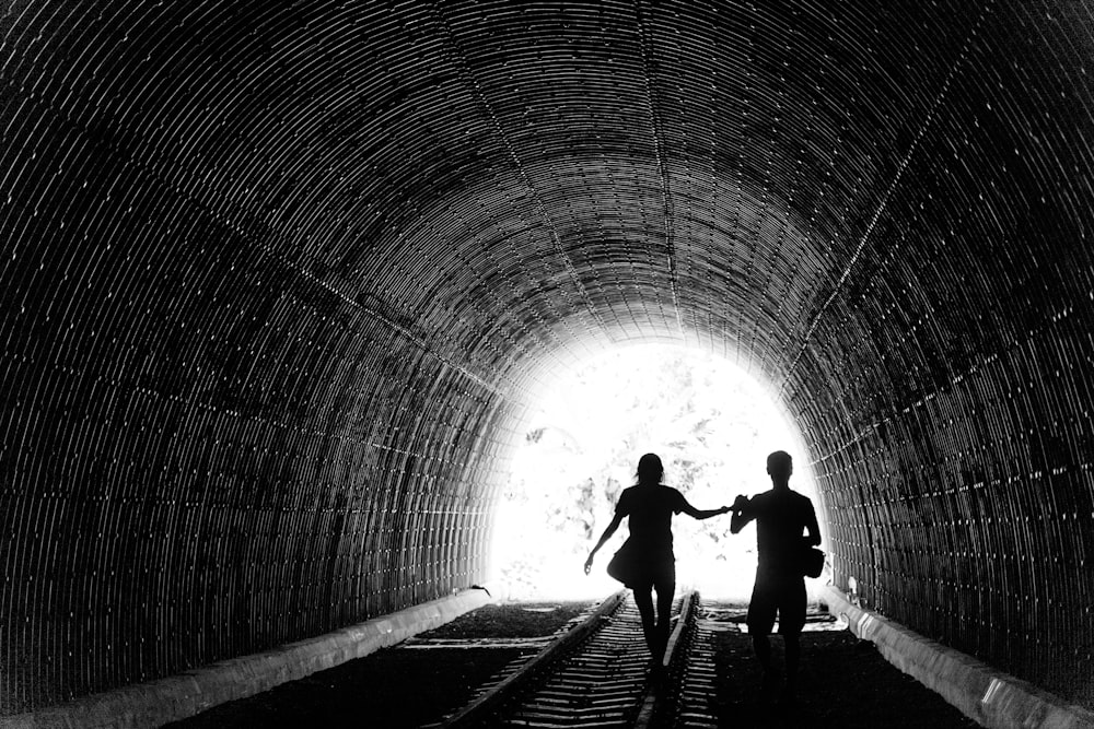 grayscale photo of man and woman holding hands inside tunnel