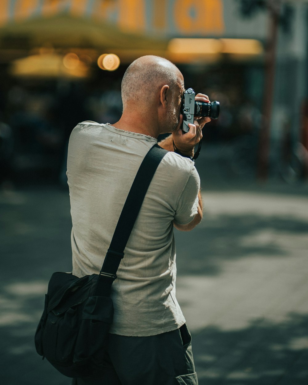 hombre con camiseta gris de cuello redondo sosteniendo una cámara DSLR