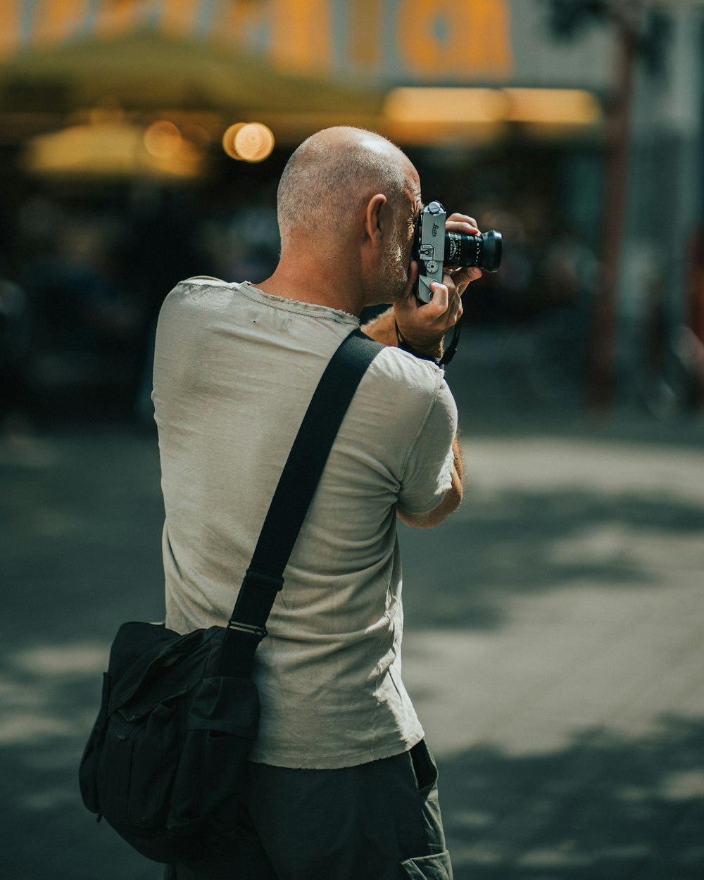 Mann trägt graues T-Shirt mit Rundhalsausschnitt und hält DSLR-Kamera in der Hand