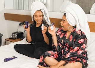 two women sitting on bed holding soft-tube