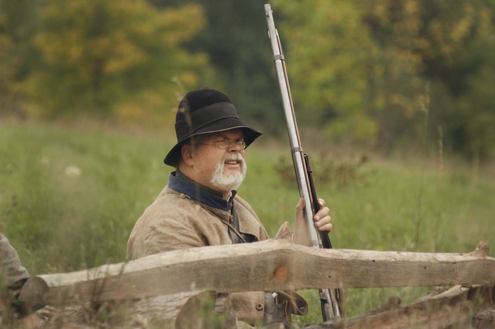 man holding hunting rifle beside wooden fence