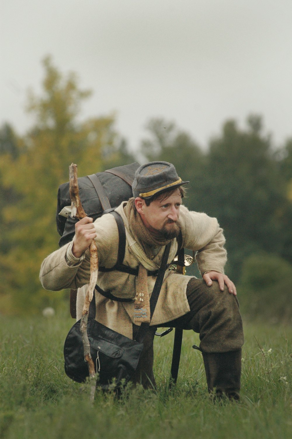 man carrying backpack and kneeling on grass field during daytime