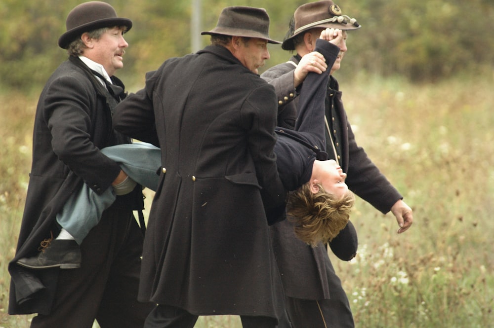 three men carrying man wearing black top