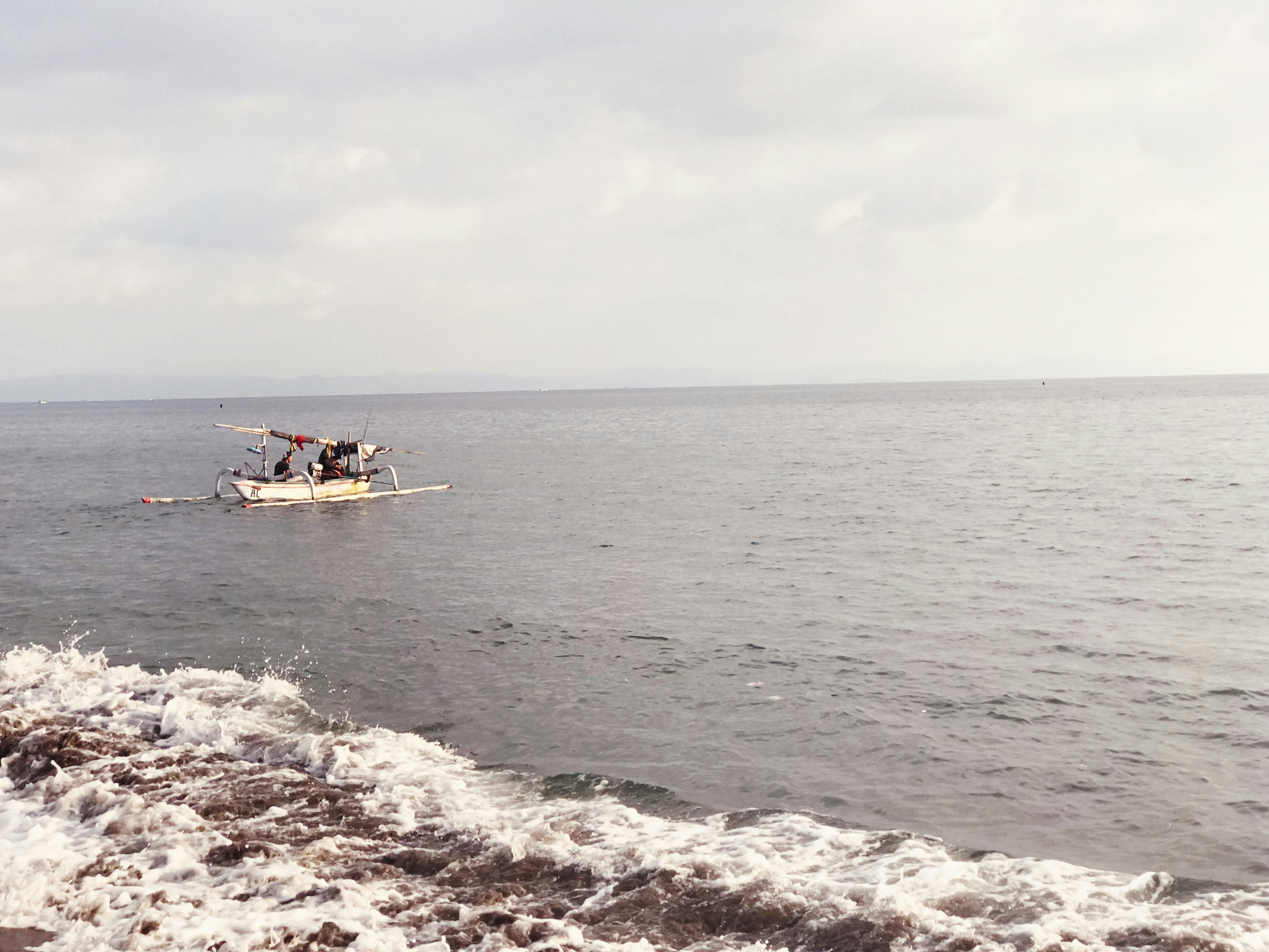 white outrigger boat leaving beach