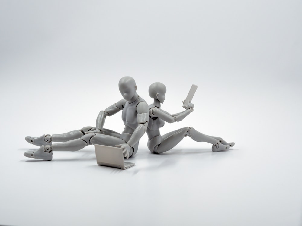 Dos figuras de acción de plástico gris sentadas en el suelo espalda con espalda